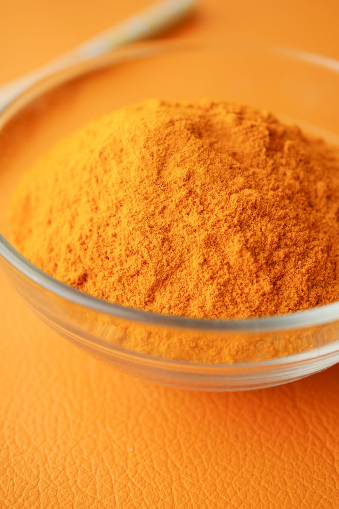 Close-up of bright turmeric powder in a glass bowl on an orange background, highlighting vibrant color contrast.