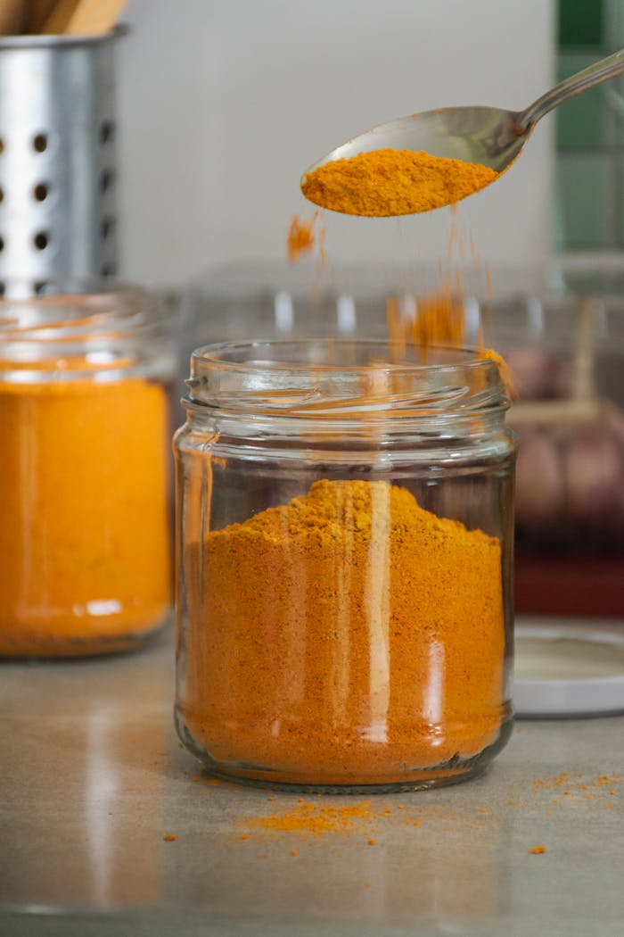 Rustic kitchen scene with turmeric powder being poured into a glass jar. Perfect for seasoning or cooking concepts.