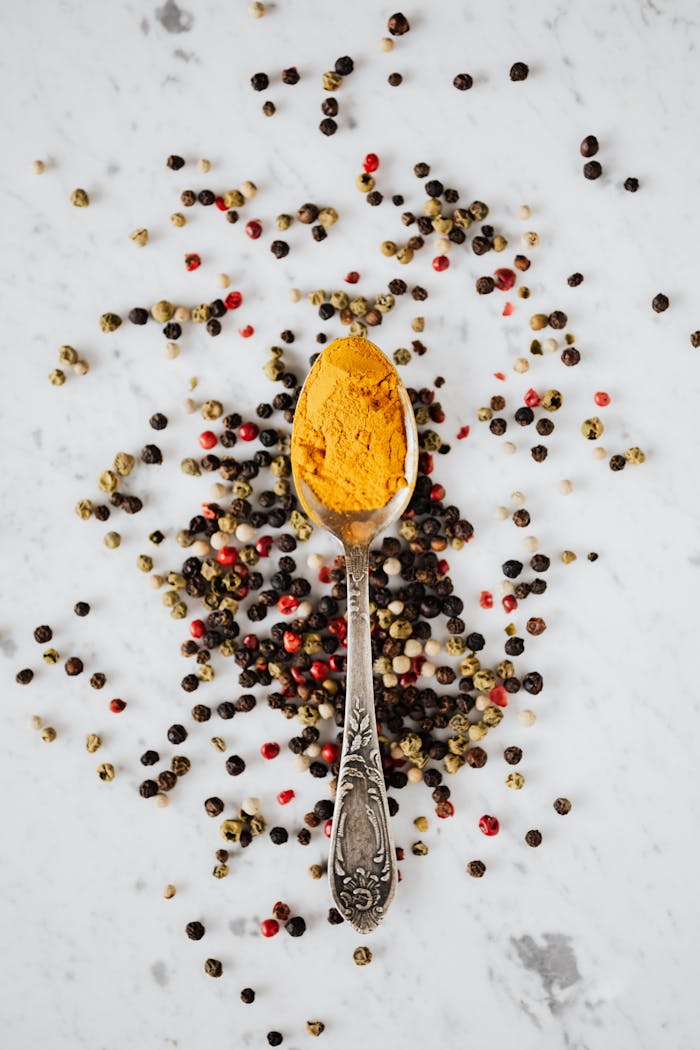 Top view of metal spoon with yellow powder on table with marble surface around assorted peppers