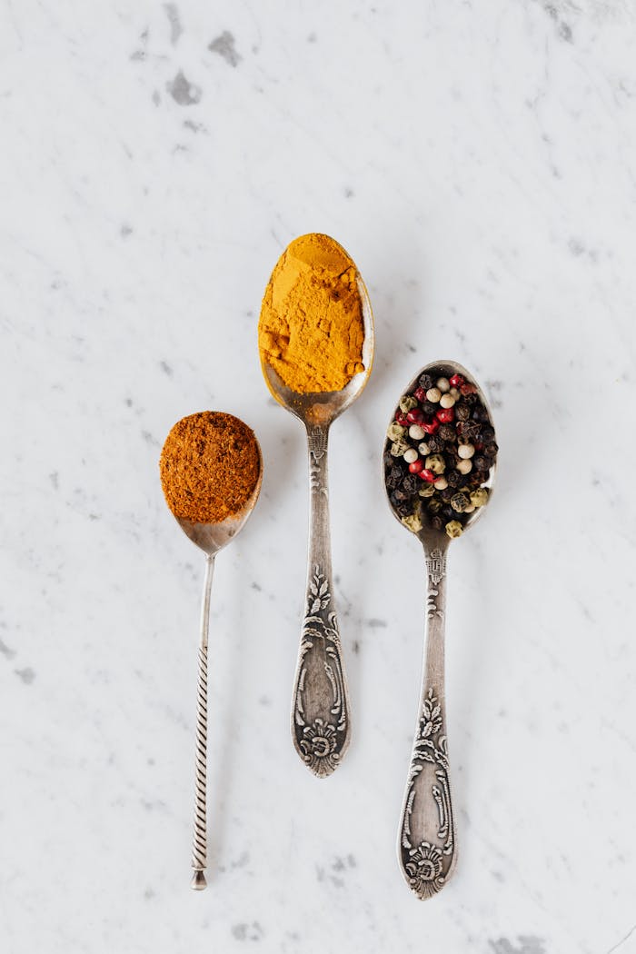 Top view composition with cinnamon and turmeric powder arranged on marble table together with mixed peppercorns used for gourmet and healthy food preparation