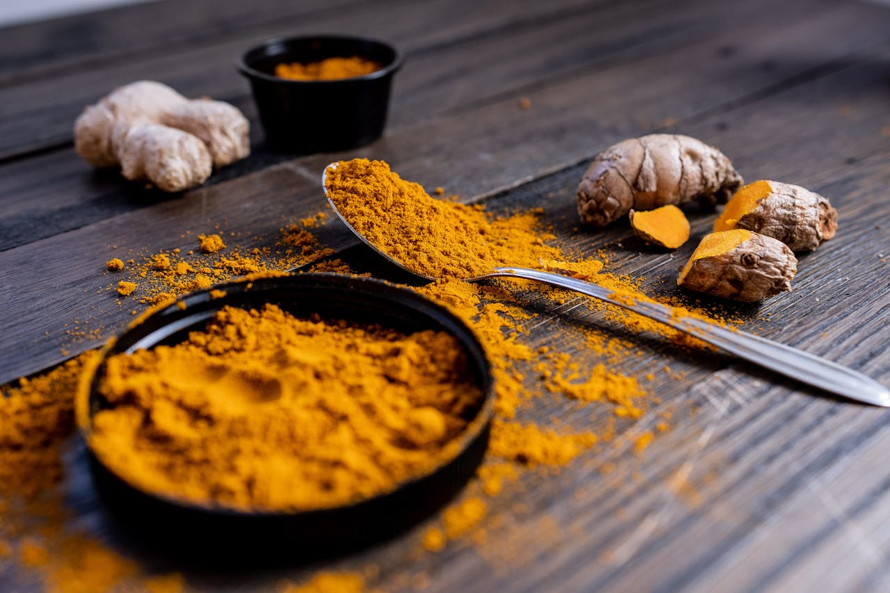 Vibrant turmeric powder and root arranged on a rustic wooden surface, showcasing culinary spice ingredients.